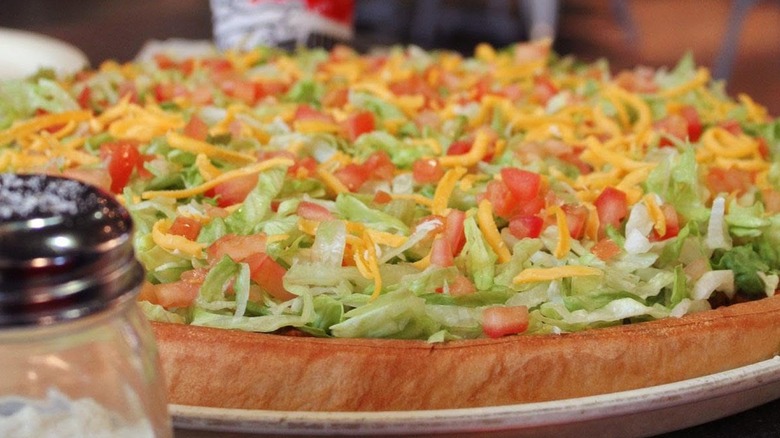 A Godfather's Pizza Chicken Taco Pie with a shaker of parmesan in the foreground