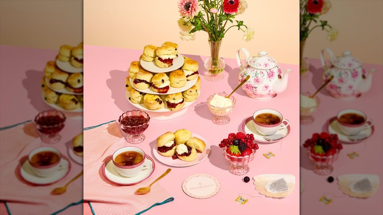 An elegant tea is set out on a pink tablecloth with scones and other accompaniments.