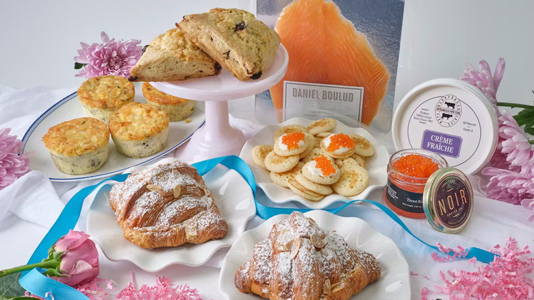 The contents of a Chef Daniel Boulud Mother's Day Brunch Gift Box spread out on a table covered with a white cloth and flowers.