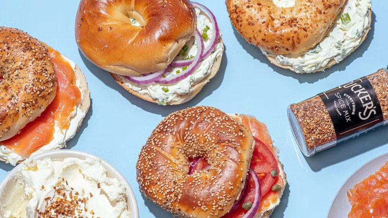 Bagel sandwiches with various toppings sit next to a container of schmear and a spice shaker.