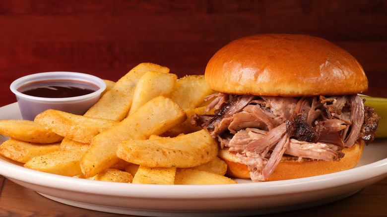 Pulled Pork Sandwich with a side of barbecue sauce and steak fries
