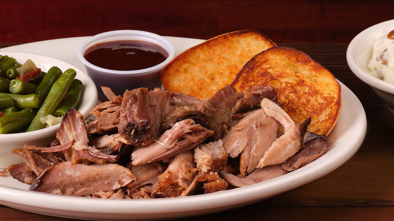 Pulled Pork dinner with a side of BBQ sauce, string bings, and toast, a bowl of mashed potatoes with gravy can barely be seen to the right