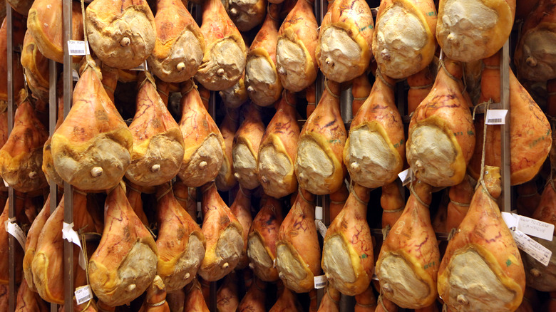 Whole prosciutto legs hanging in a curing room