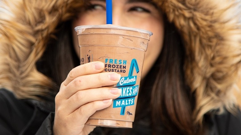 Person wearing fur coat, holding Culver's milkshake
