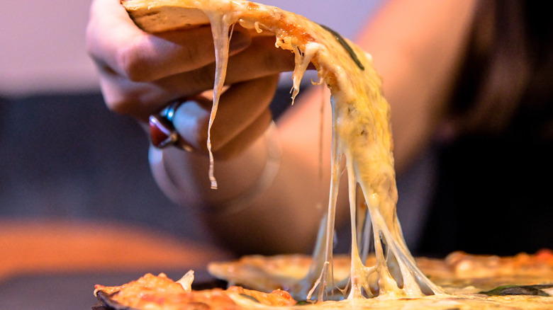Person grabbing cheesy pizza slice