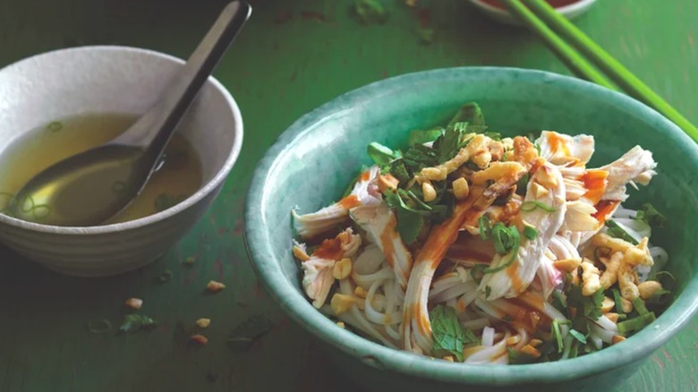 Bowl of soup next to a green bowl of pulled chicken and rice noodles