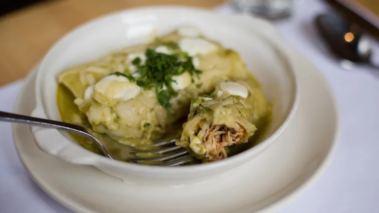 Enchiladas in green salsa in bowl with garnish