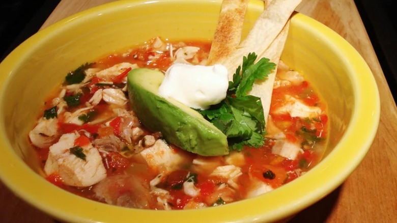Chicken tortilla soup in yellow bowl on wooden counter