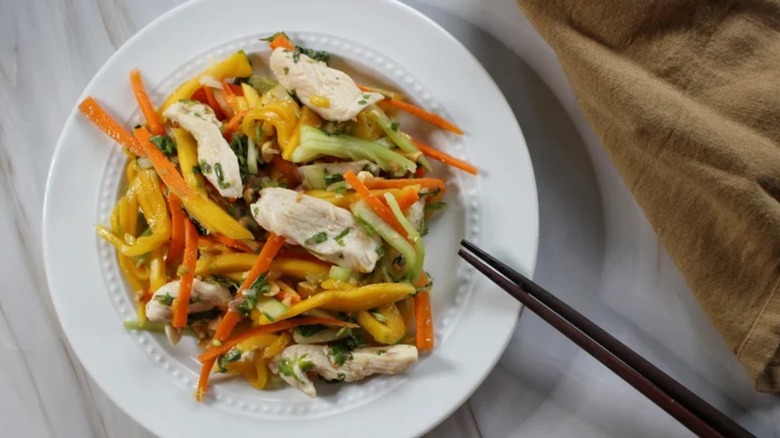 Shredded mango salad with chicken in white bowl