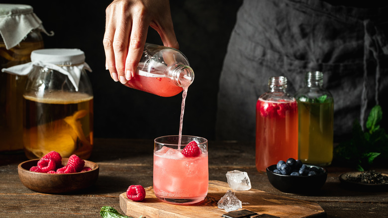 hand pouring kombucha into glass