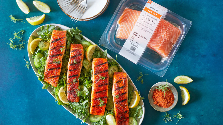 A package of Trader Joe's BBQ Cut Fresh Atlantic Salmon Fillets sits next to a platter of cooked salmon.