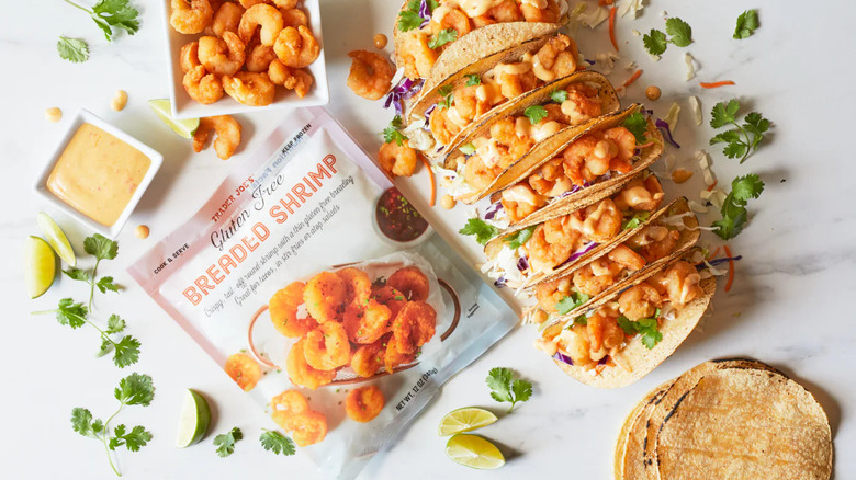 A package of Trader Joe's Gluten Free Breaded Shrimp next to shrimp tacos, sauce, and a dish of prepared shrimp.