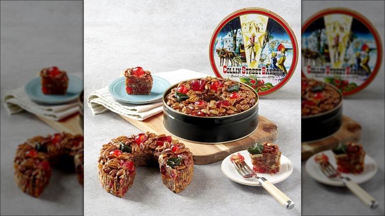 A Collin Street Bakery fruitcake sits on a serving board, while another sits adjacent with a removed piece sitting on a nearby plate
