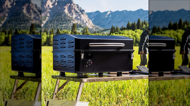 A Traeger Trailhead Wood Pellet Grill sits on a portable table in a mountain setting