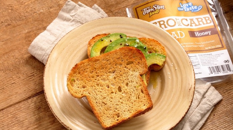 A package of ThinSlim Foods Zero Net Carb Honey Bread sits adjacent to a plate with two slices of bread and sliced tomato