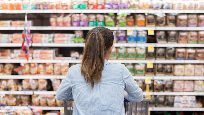 A shopper with a shopping cart scans plentiful bread options in a supermarket