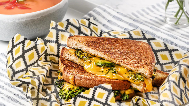 A grilled cheese sandwich on Nature's Own Life Wheat Plus Protein Bread sits on a colorful napkin next to a bowl of tomato soup