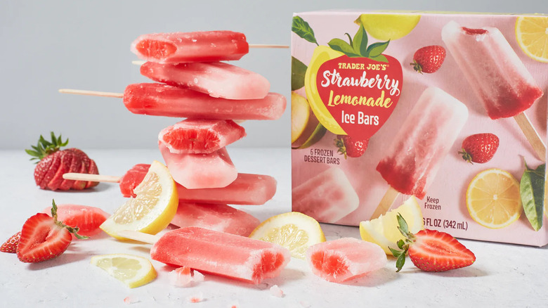 A box of Trader Joe's Strawberry Lemonade Ice Bars next to a stack of the ice pops, lemon wedges, and cut strawberries.
