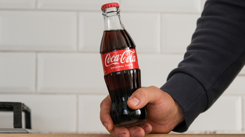A hand holds a glass bottle of Coca-Cola