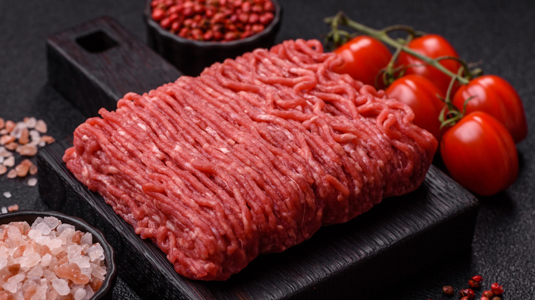 Raw ground beef in a rectangle shape with small tomatoes and pink rock salt on either side.