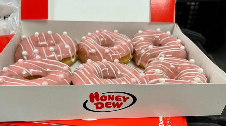 Six pink frosted donuts with white and pink pearls in a white and red Honey Dew Donuts box