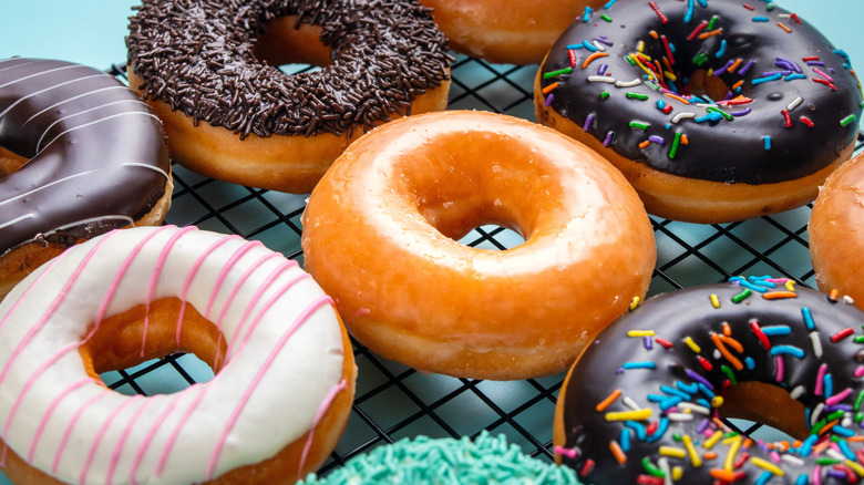 Several donuts with different frostings, including chocolate, vanilla, and glazed, on a rack over a light green surface