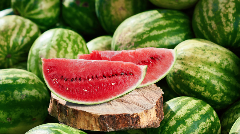 2 wedges of watermelon surrounded by numerous whole watermelons