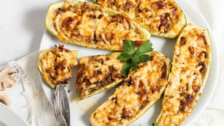 White plate with two cheesy mushroom-stuffed zucchini boats