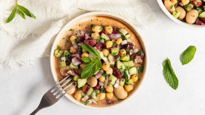 Shallow white bowl filled with three bean salad and fresh herbs