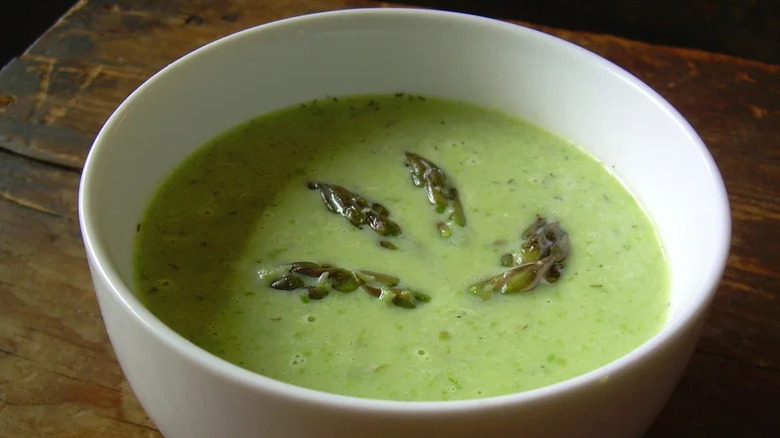 White bowl of asparagus soup with fresh spears