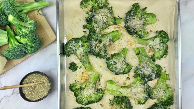 Baking tray of smashed broccoli topped with grated Parmesan and seasoning
