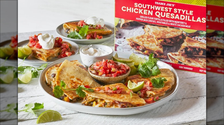 Plates of prepared Trader Joe's Southwest Style Chicken Quesadillas, with toppings and garnishes, sit next to a product package.