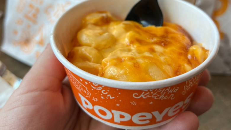 A hand holds a cup of Mac & Cheese from Popeyes