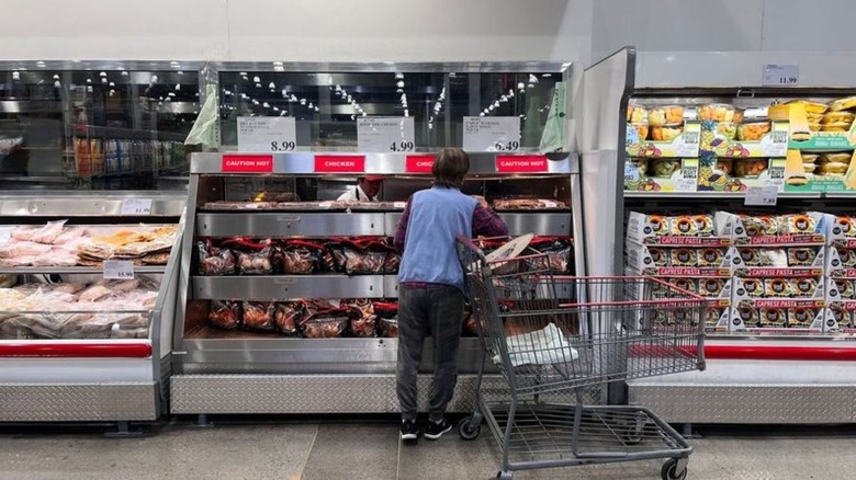 A person is looking at the rotisserie chicken display inside Costco.