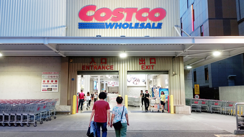 Two people are walking into a Costco storefront.