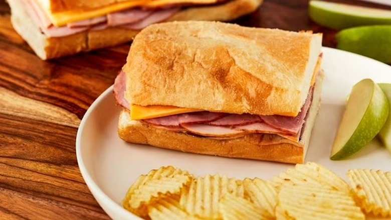 Half a Marketside Supreme Sub Sandwich on a plate with chips and sliced apple.