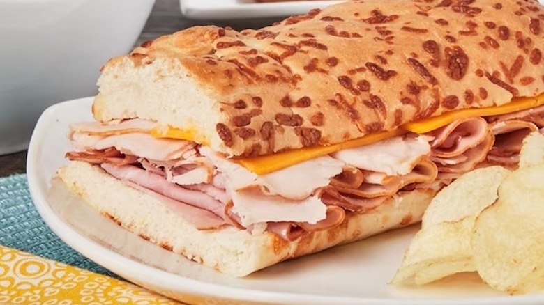 Half a Marketside All American Sub Sandwich sitting on a plate with potato chips.