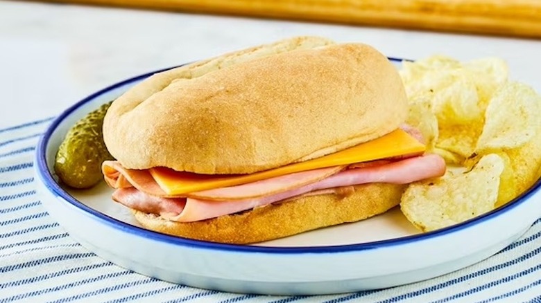 Marketside Smoked Ham & Cheddar Mini Sub Sandwich sitting on a plate with chips and a pickle.