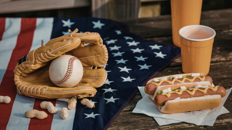 Two hot dogs sit next to a beverage and a baseball mitt with a ball in it.