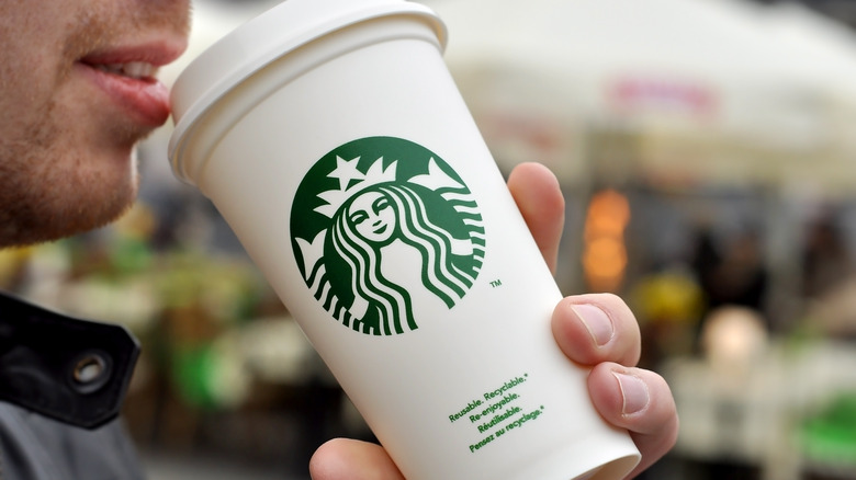 Close up of a man drinking from a white Starbucks coffee cup