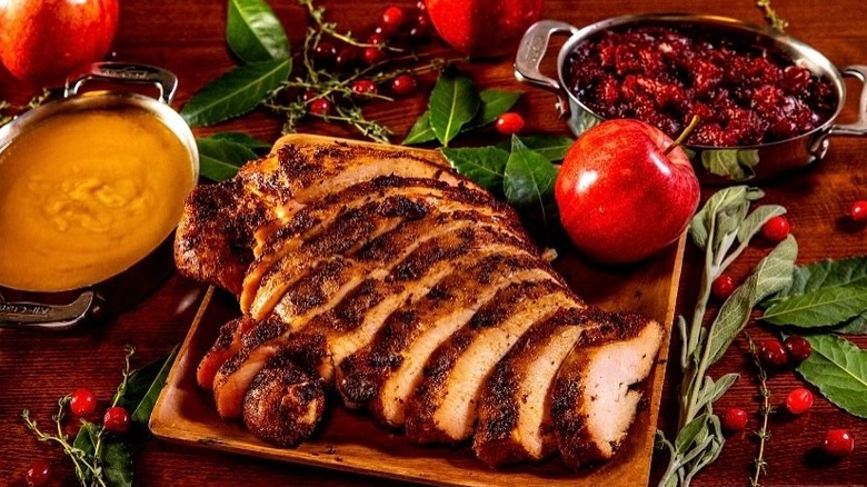 Platter of sliced turkey breast beside gravy and cranberry sauce with decorative arrangements