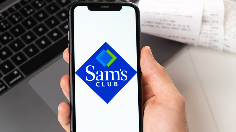 A hand holds a mobile phone with the Sam's logo showing.
