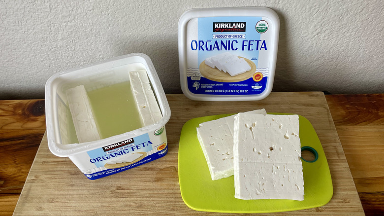 Open container of Kirkland Signature Organic Feta with slabs pulled out on a cutting board