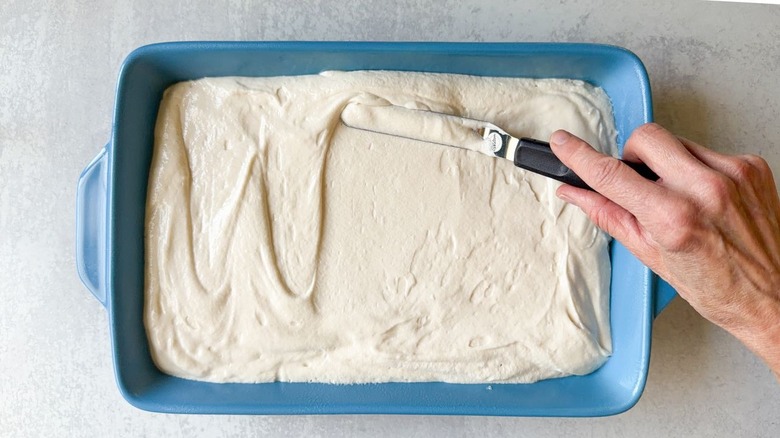 Spreading vanilla cake batter in a blue baking pan with an offset spatula