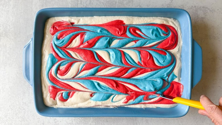 Swirling together red, white, and blue cake batters in blue baking dish with tip of knife
