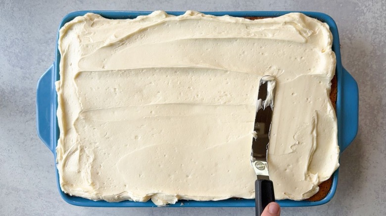 Spreading vanilla icing on cake in 13 x 9-inch pan
