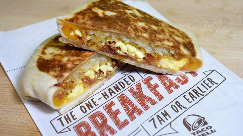 A Taco Bell Breakfast Crunchwrap sits in two pieces on a paper bag