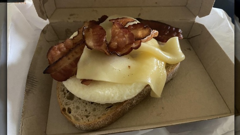A Dunkin' Donuts Sourdough Breakfast Sandwich without a top slice of bread sits in a cardboard sandwich box