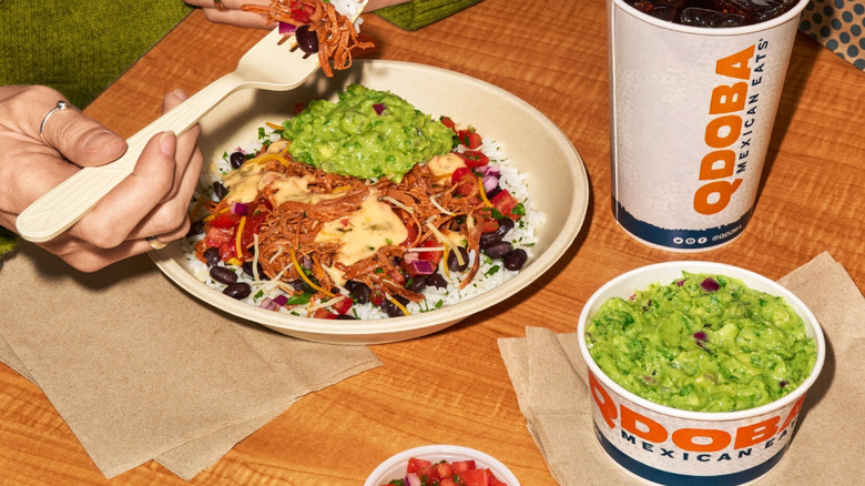 Person eating a Qdoba bowl with a fountain drink