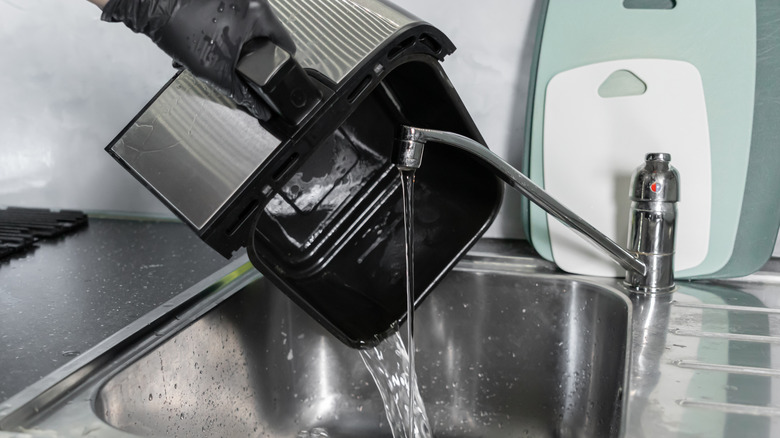 Someone washes an air fryer basket in sink.